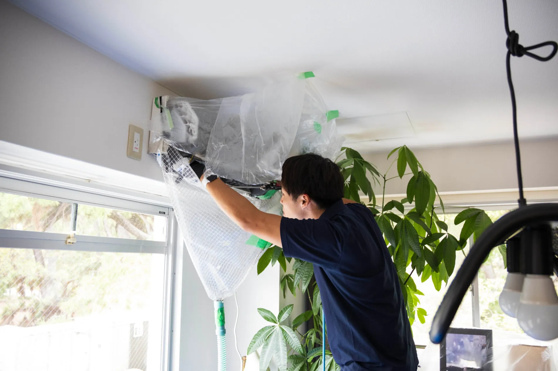 植物のある室内でエアコンクリーニングの養生作業をするN.Nスタイルのスタッフ